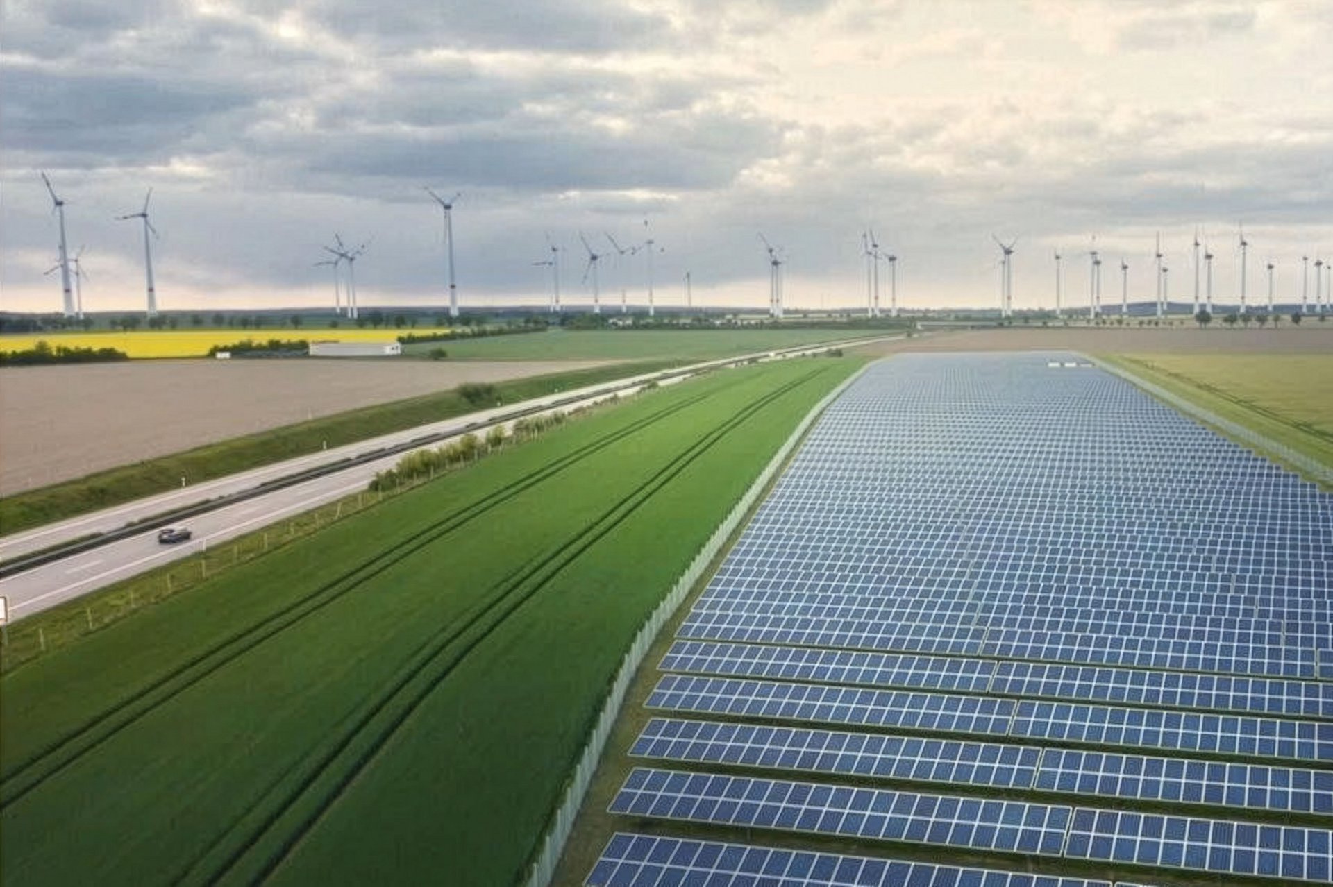PV-Anlage neben einer Autobahn, im Hintergrund sind Windkraftanlagen zu sehen